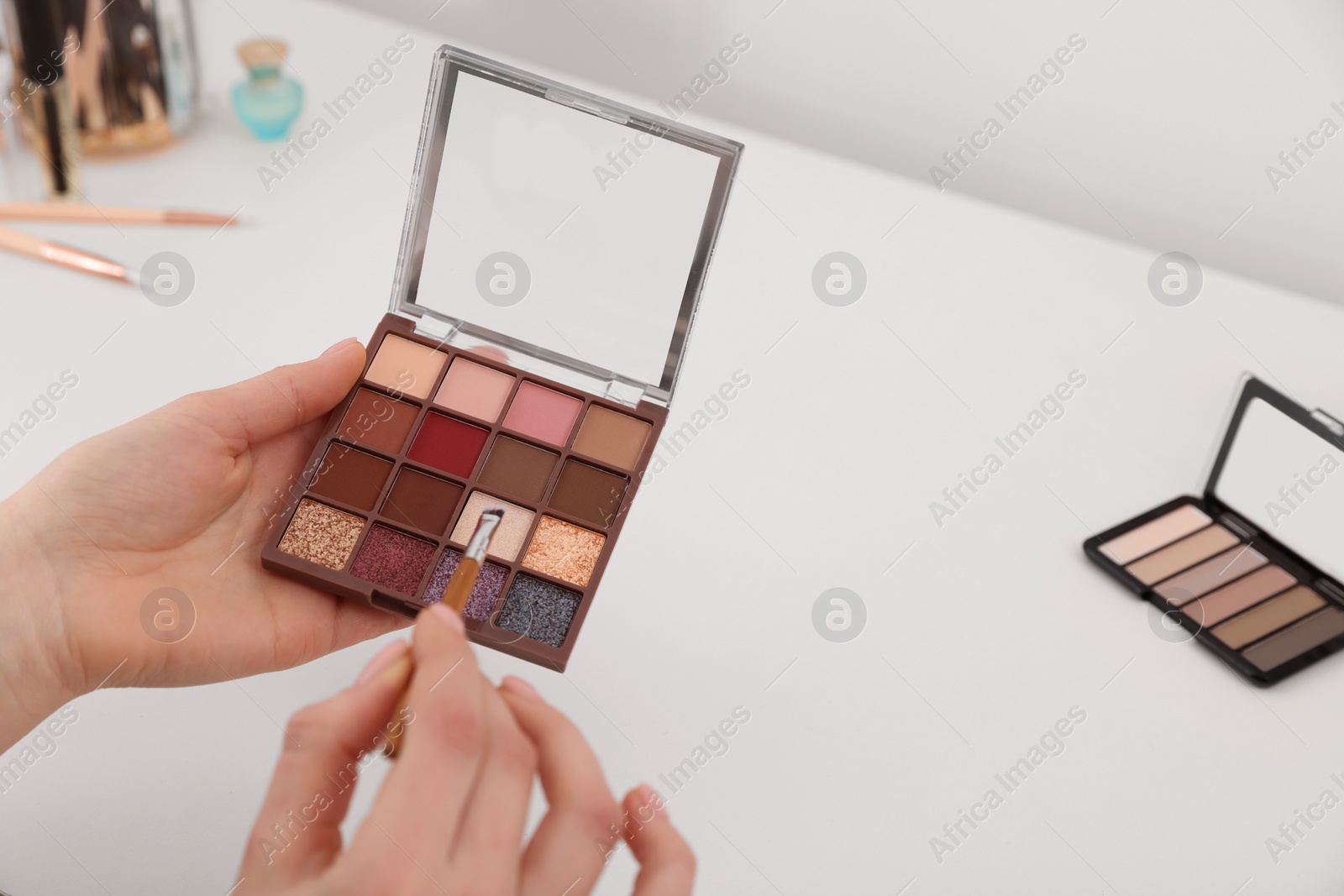 Photo of Woman with eyeshadow palette and brush at dressing table, closeup