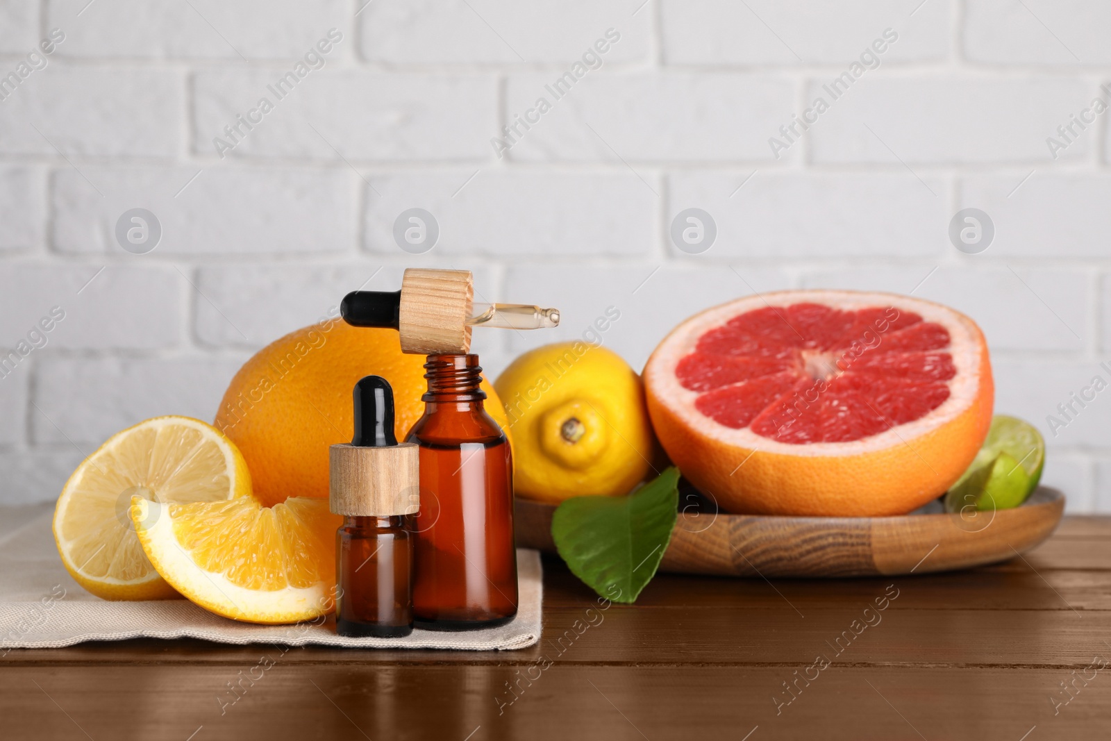 Photo of Bottles of essential oils with different citrus fruits and leaf on wooden table against white brick wall