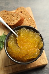 Photo of Fresh pike caviar in bowl and bread on grey table, closeup