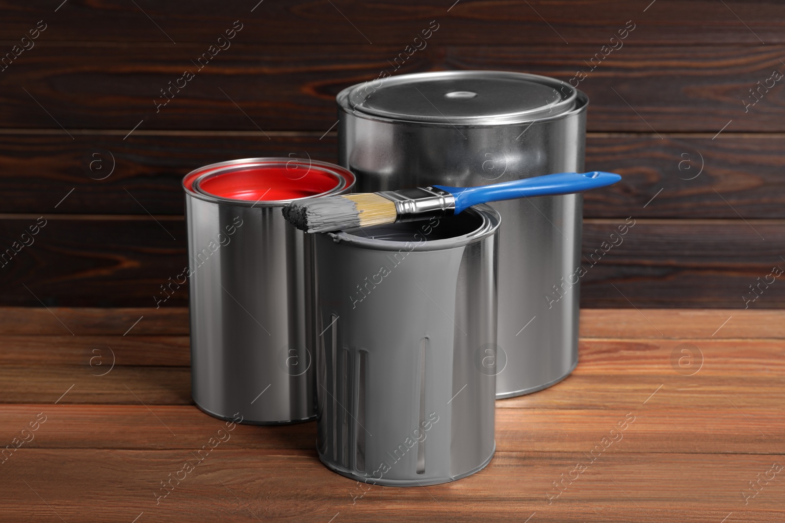 Photo of Cans of paints and brush on wooden table