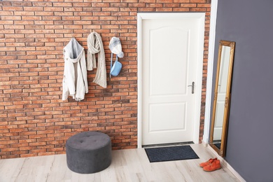 Photo of Stylish hallway interior with door and clothes hanging on brick wall