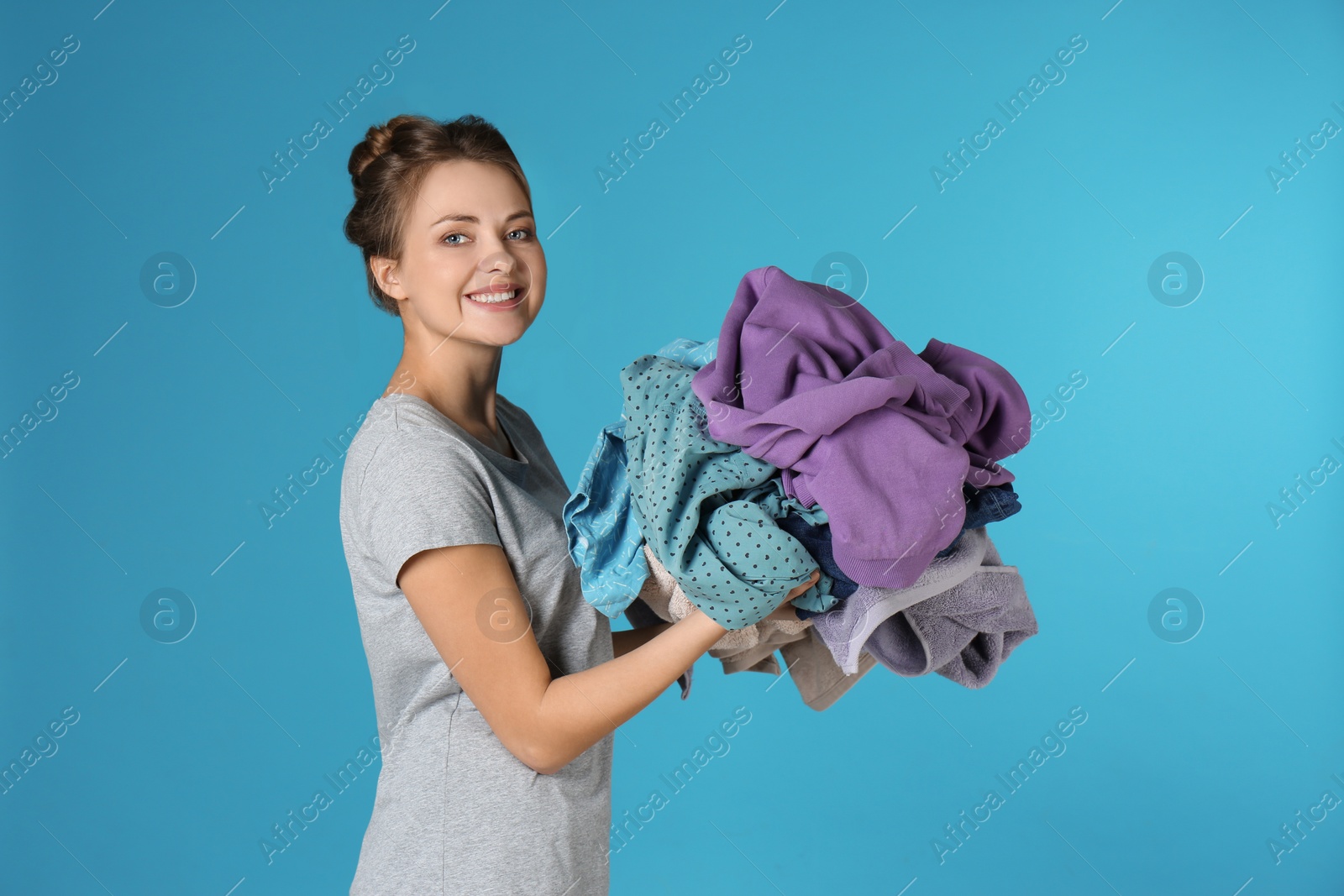 Photo of Happy young woman holding pile of dirty laundry on color background