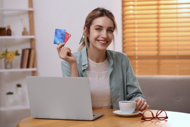 Photo of Woman with credit cards using laptop for online shopping at wooden table indoors