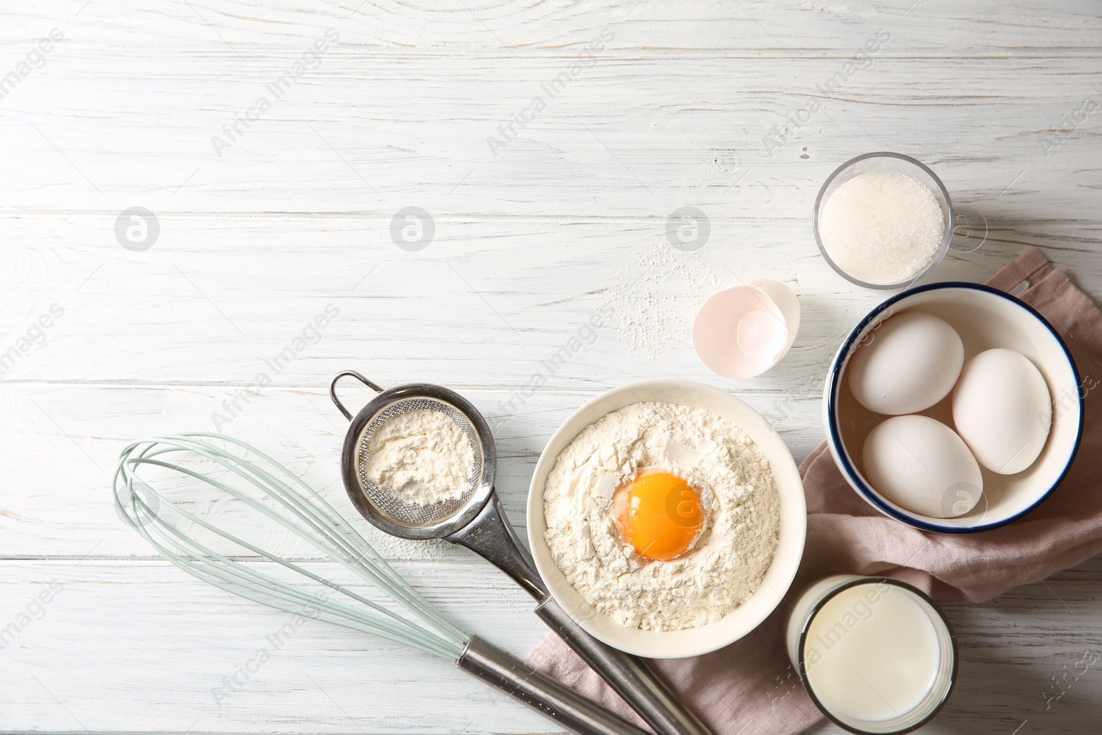 Photo of Flour with yolk in bowl and other ingredients for dough on white wooden table, flat lay. Space for text