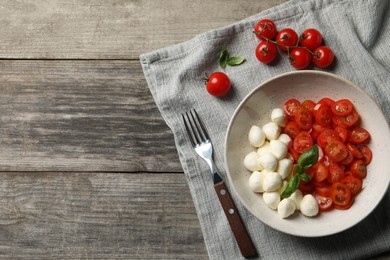 Delicious mozzarella balls, tomatoes and fork on wooden table, flat lay. Space for text