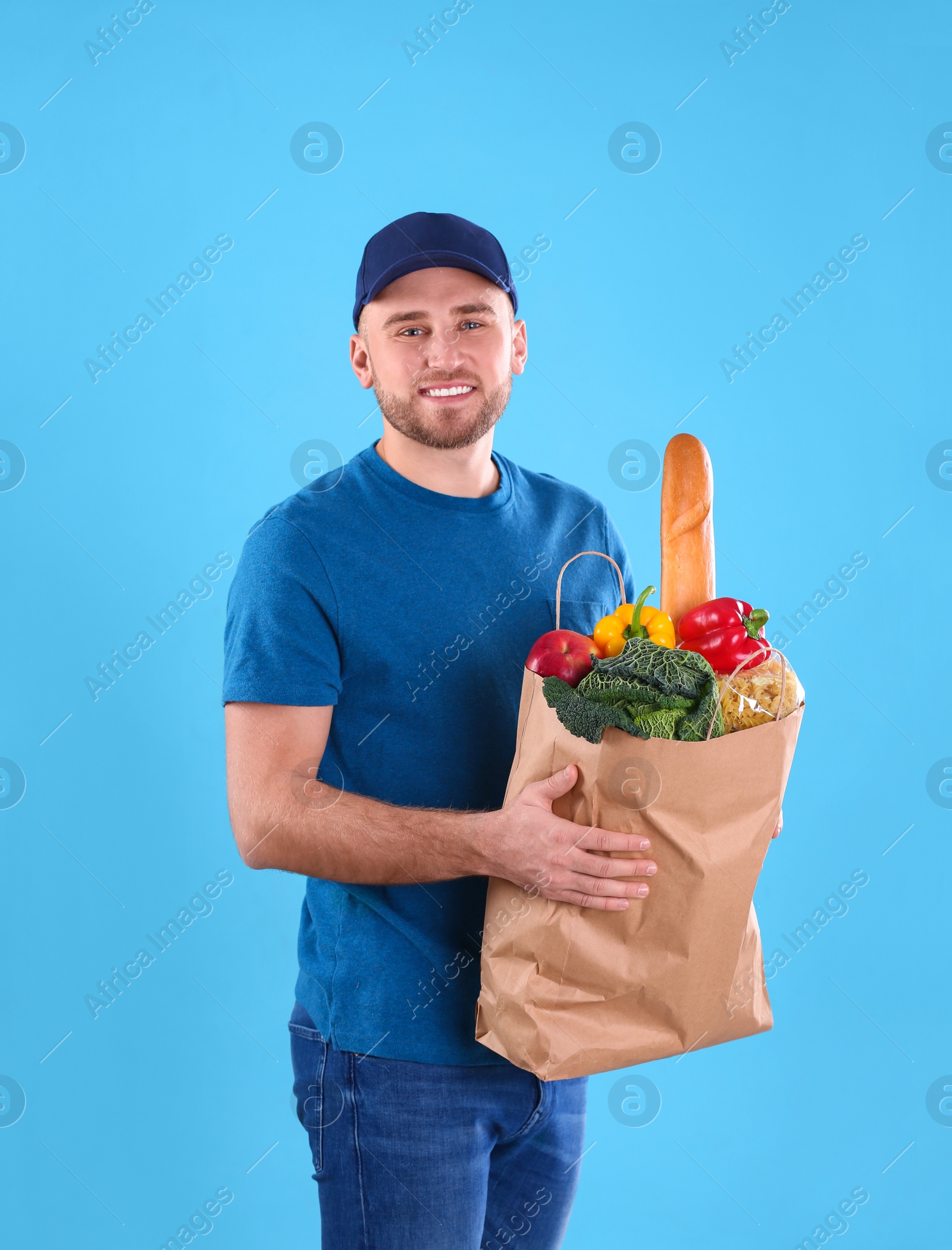 Photo of Delivery man holding paper bag with food products on color background