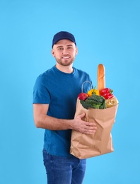 Photo of Delivery man holding paper bag with food products on color background