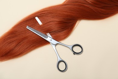 Photo of Professional hairdresser scissors and hair strand on beige background, flat lay. Haircut tool