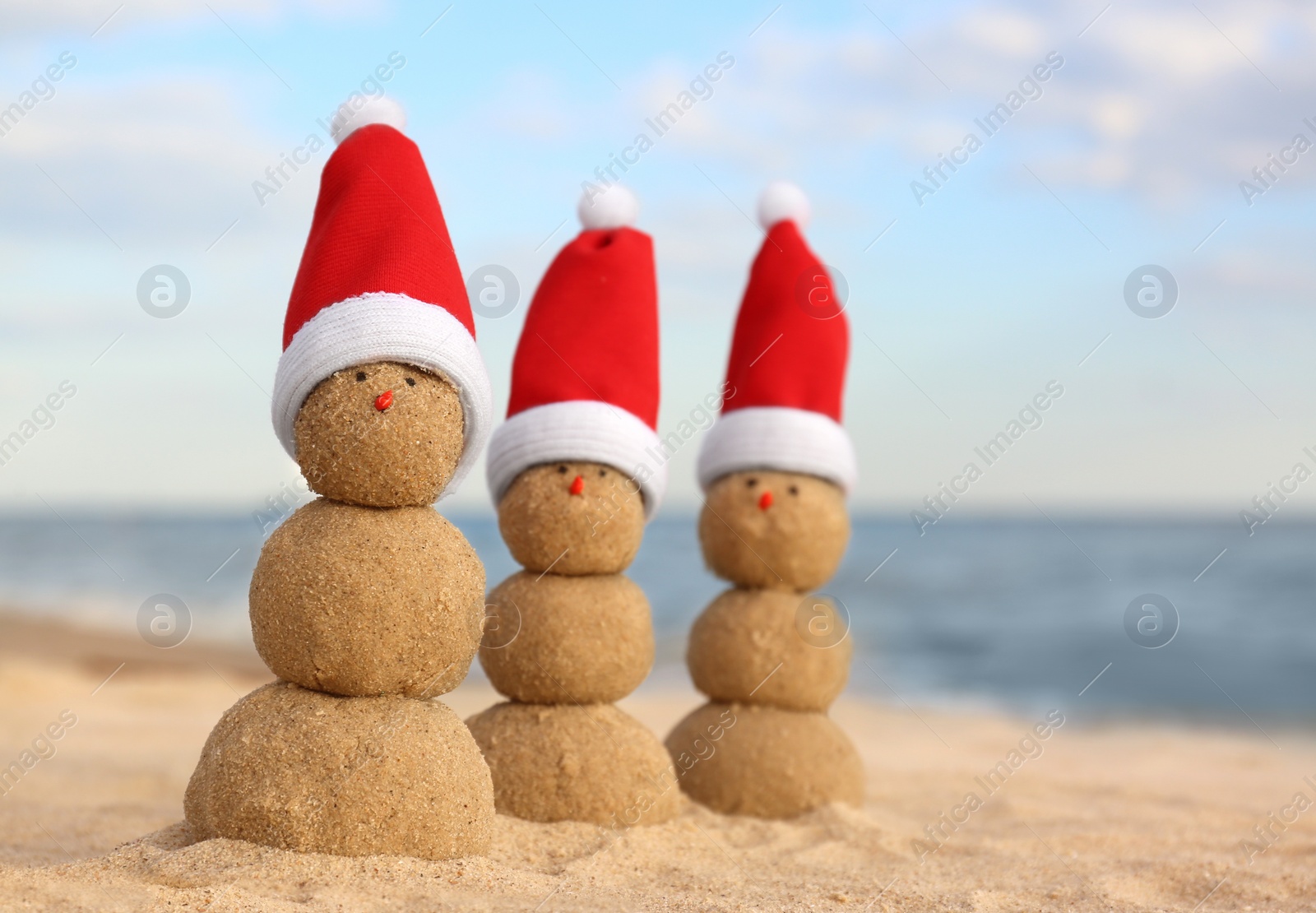 Photo of Snowmen made of sand with Santa hats on beach near sea. Christmas vacation