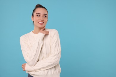 Beautiful young woman in stylish warm sweater on light blue background, space for text