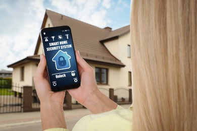 Image of Woman using home security system application on smartphone outdoors, closeup