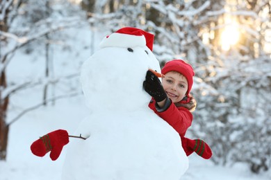 Photo of Cute little boy making snowman in winter park