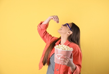 Young woman with 3D glasses eating tasty popcorn on color background