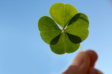 Photo of Woman holding green clover leaf against blurred background, closeup