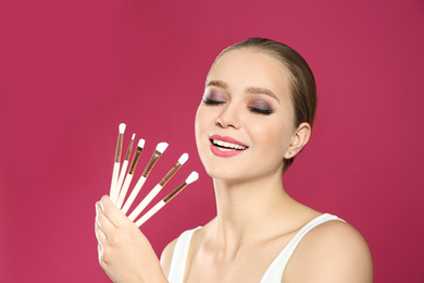 Beautiful woman with makeup brushes on pink background