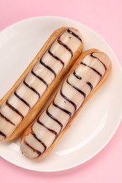 Photo of Delicious eclairs covered with glaze on pink background, top view