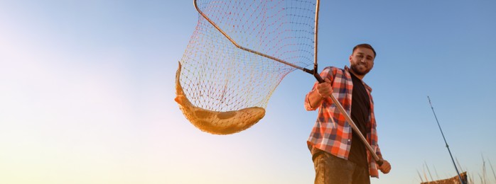 Image of Fisherman holding fishing net with catch against blue sky, space for text. Banner design