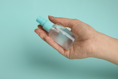 Photo of Woman holding antiseptic spray on light blue background, closeup