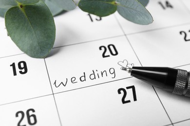 Photo of Calendar with date reminder about Wedding Day, pen and green leaves, closeup