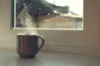 Cup of hot drink near window on rainy day. Space for text