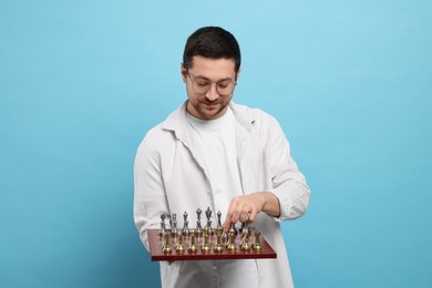 Photo of Handsome man holding chessboard with game pieces on light blue background