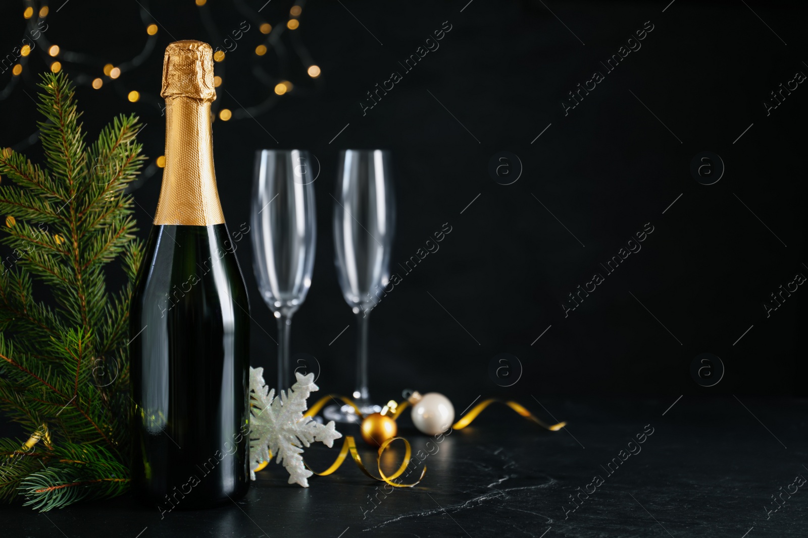 Photo of Happy New Year! Bottle of sparkling wine, glasses and festive decor on black background, space for text