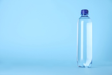 Photo of Plastic bottle with water on light blue background, space for text