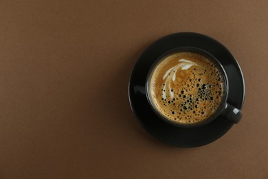 Cup of tasty coffee on brown background, top view. Space for text