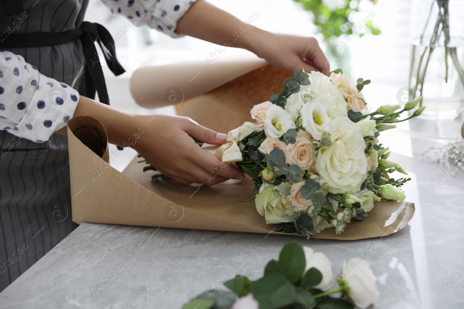 Photo of Florist wrapping beautiful wedding bouquet with paper at light grey marble table, closeup