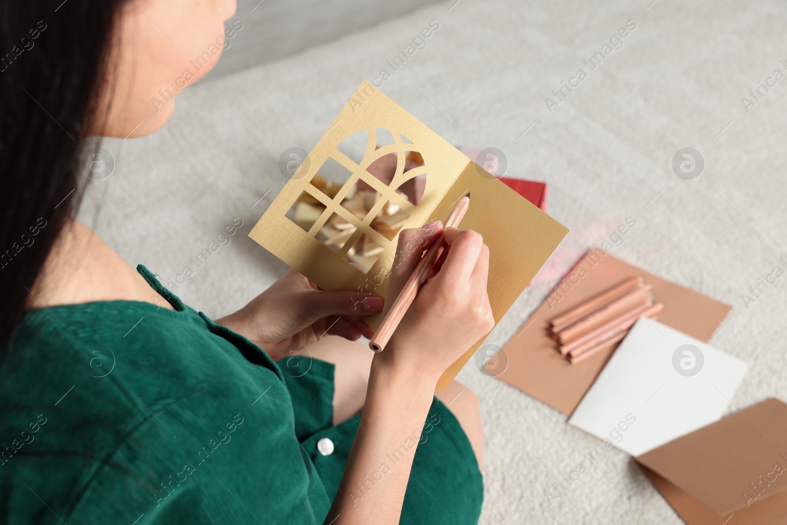 Photo of Woman writing message in greeting card on floor in living room, closeup