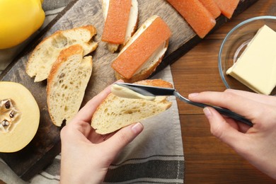 Photo of Making sandwich with quince paste. Woman buttering bread at wooden table, top view