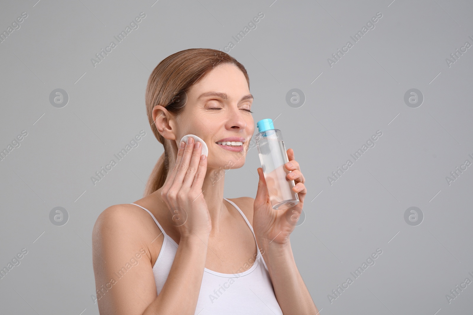 Photo of Beautiful woman removing makeup with cotton pad on gray background, space for text