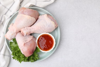 Fresh marinade, raw chicken drumsticks and lettuce on light table, top view. Space for text