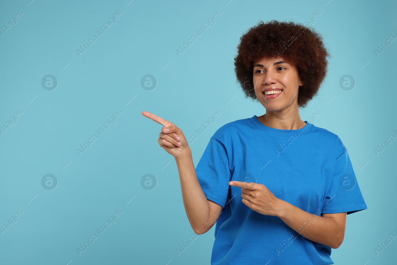 Photo of Happy young woman pointing at something on light blue background. Space for text