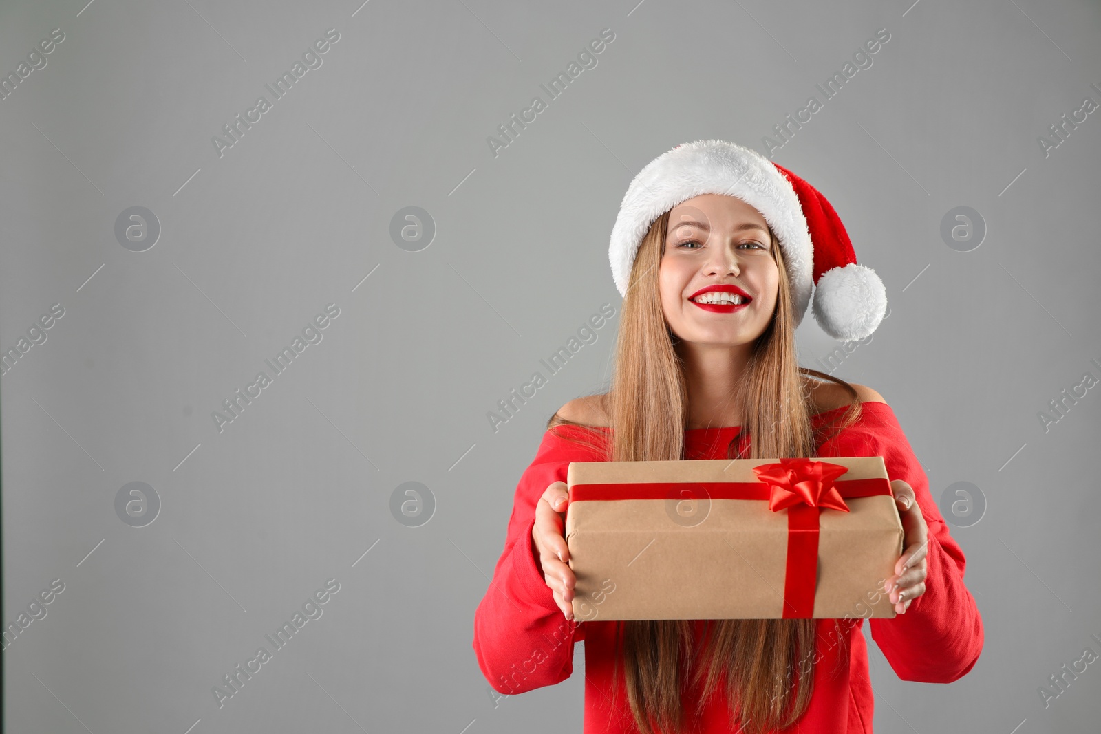 Photo of Young beautiful woman in Santa hat with gift box on grey background. Christmas celebration