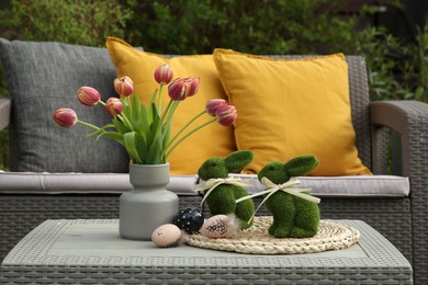 Photo of Terrace with Easter decorations. Bouquet of tulips in vase, bunny figures and decorated eggs on table outdoors