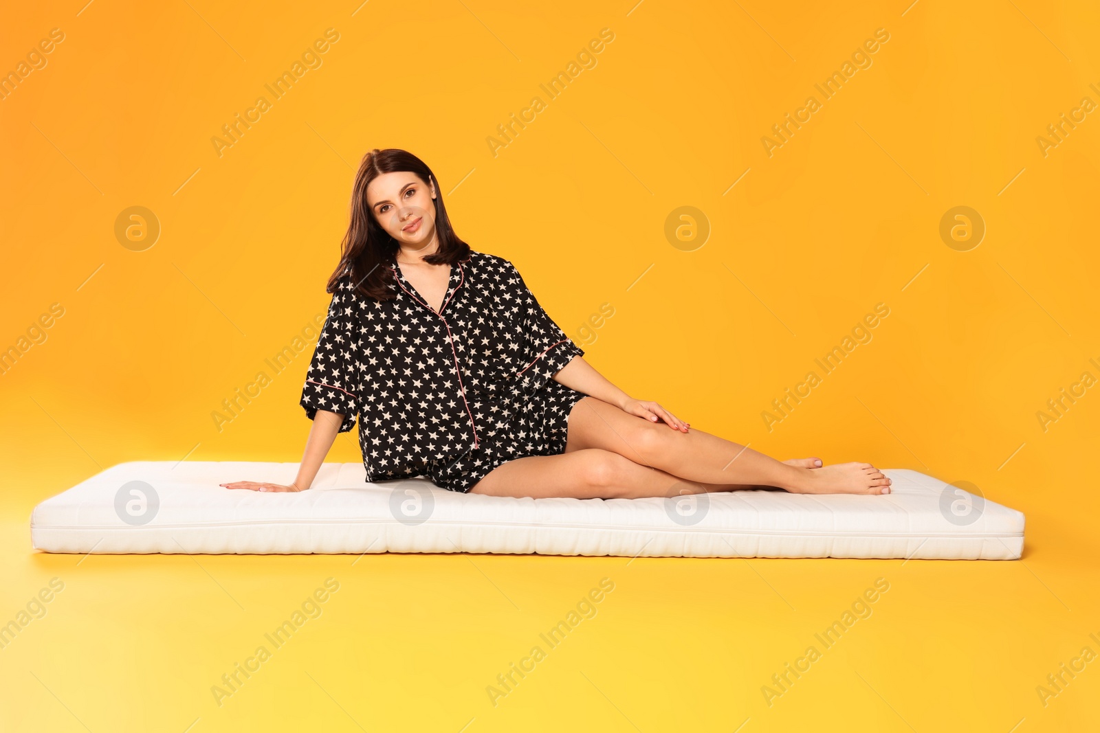 Photo of Young woman sitting on soft mattress against orange background