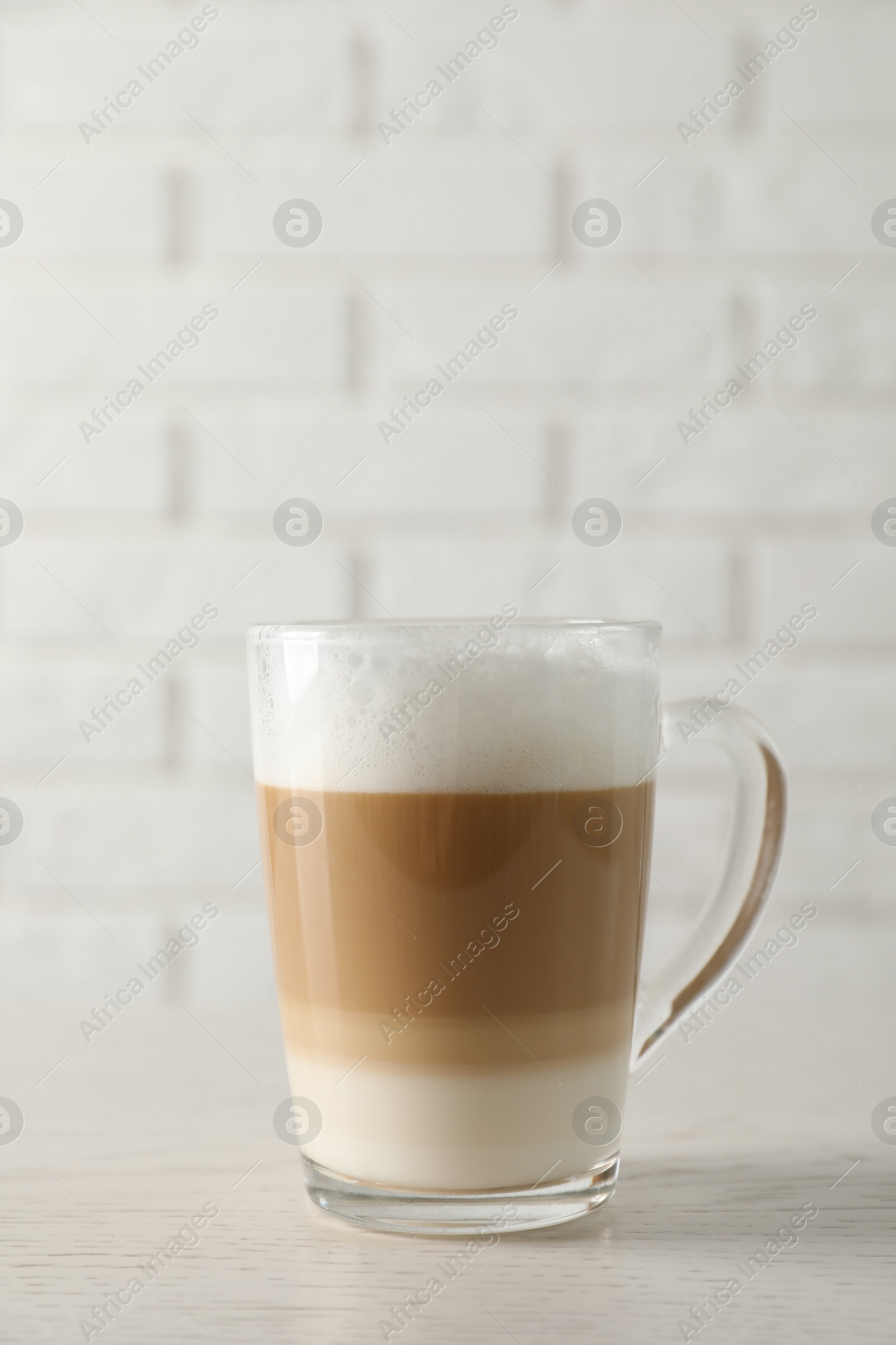 Photo of Hot coffee with milk in glass cup on white wooden table