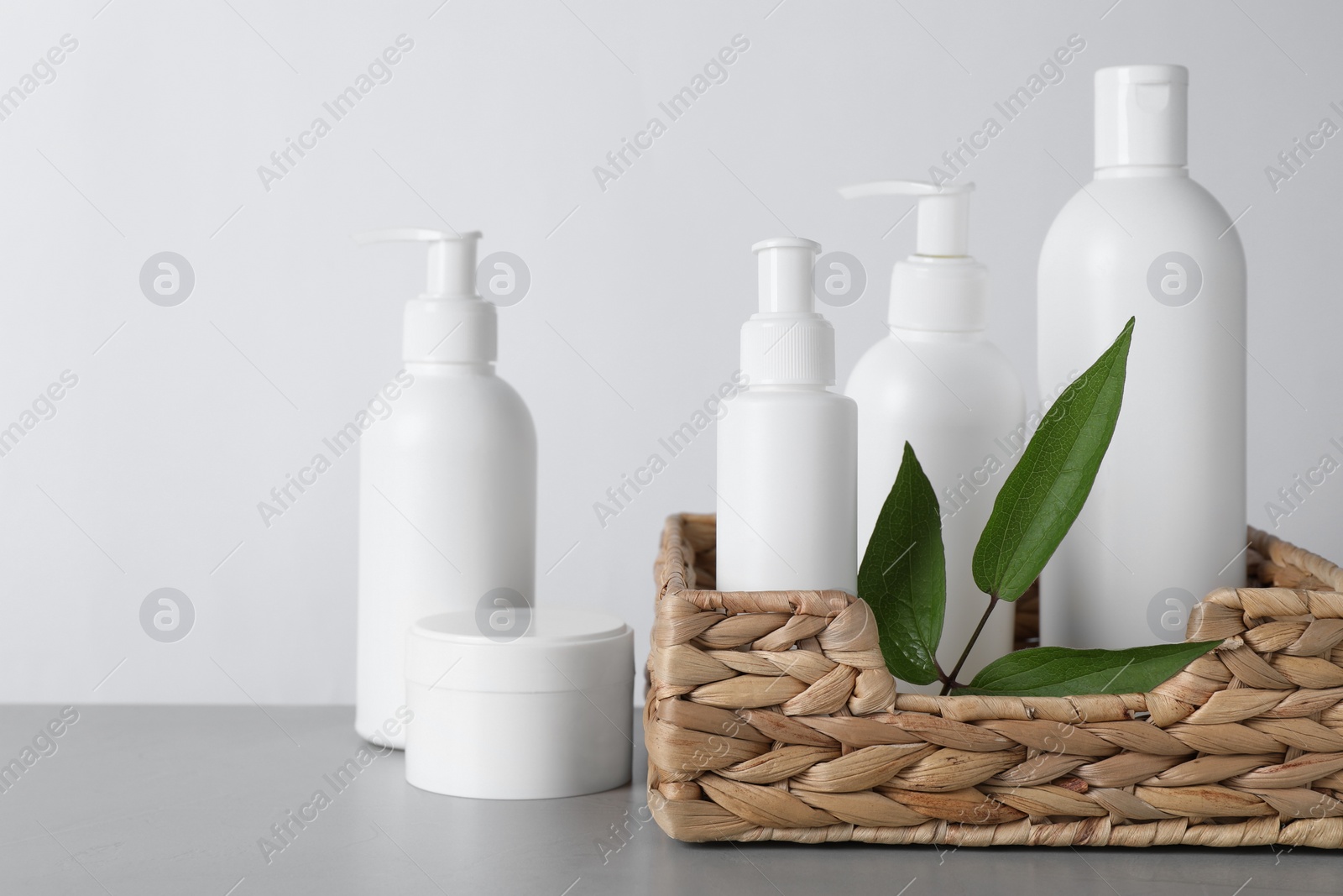 Photo of Different cosmetic products and leaves on grey table. Space for text