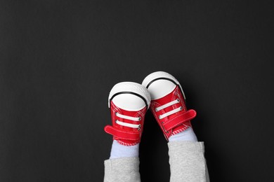 Photo of Little child in stylish red gumshoes on black background, top view