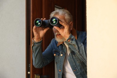 Photo of Concept of private life. Curious senior man with binoculars spying on neighbours outdoors