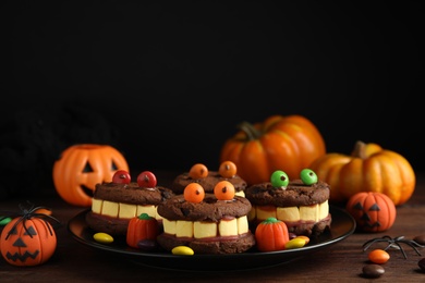 Photo of Delicious desserts decorated as monsters on wooden table. Halloween treat