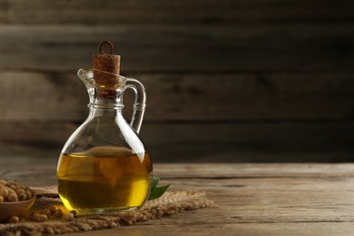 Photo of Glass jug of oil and soybeans on wooden table. Space for text