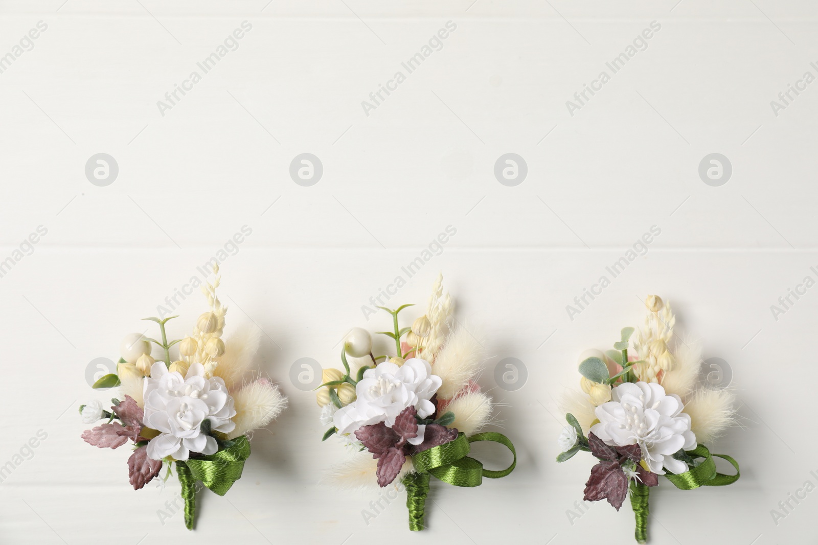 Photo of Beautiful boutonnieres on white background, flat lay. Space for text