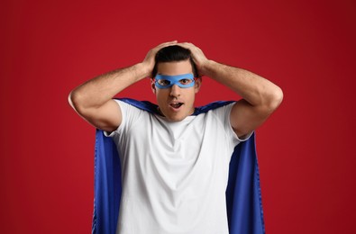 Emotional man wearing superhero cape and mask on red background