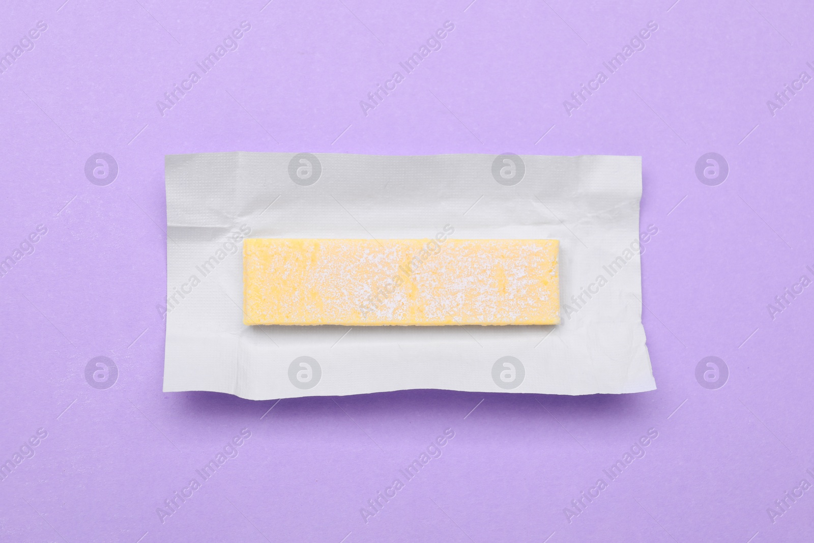 Photo of Unwrapped stick of chewing gum on violet background, top view