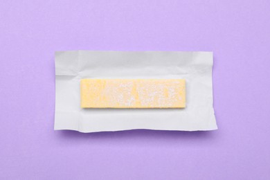 Photo of Unwrapped stick of chewing gum on violet background, top view