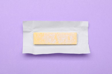 Unwrapped stick of chewing gum on violet background, top view