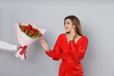 Happy woman receiving red tulip bouquet from man on light grey background. 8th of March celebration