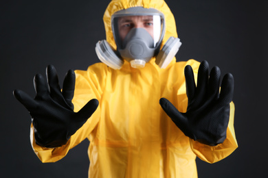 Photo of Man in chemical protective suit making stop gesture against black background, focus on hands. Virus research